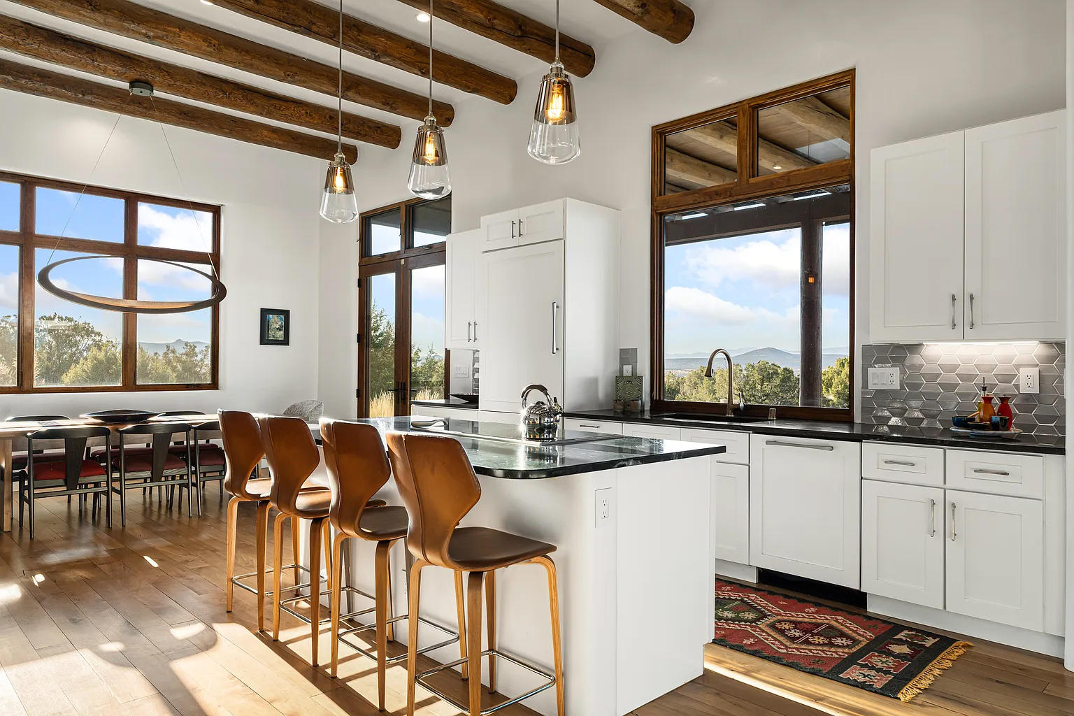 Open custom kitchen and dining space in Santa Fe with island seating, vigas and mountain views