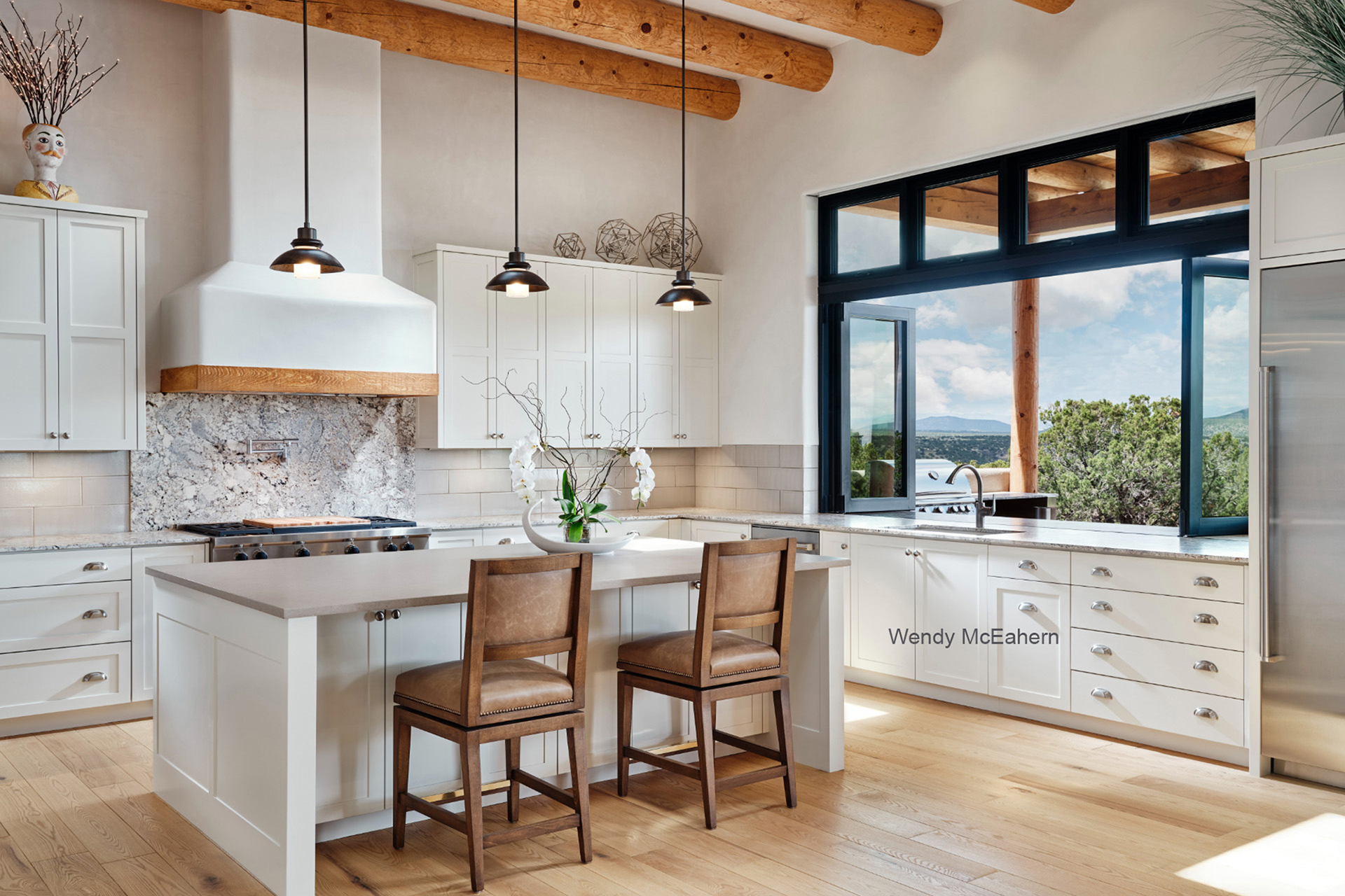 Light-filled Santa Fe kitchen with white cabinetry, vigas and expansive high-desert views